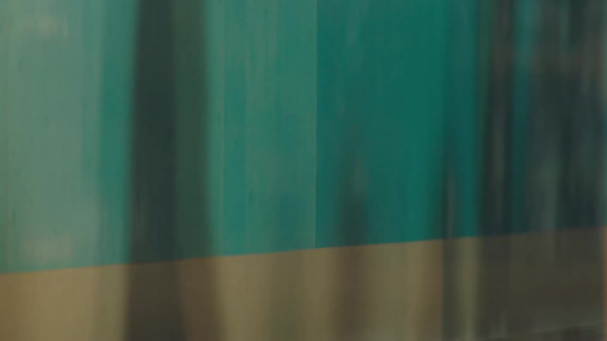 A close-up side view of a speeding teal and cream train car creates an abstract motion blur effect