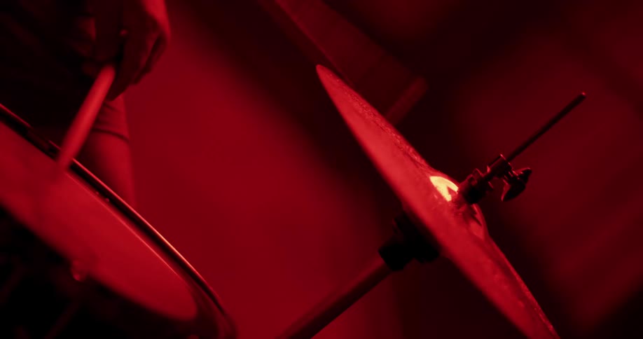 Energetic drummer strikes a cymbal with drumsticks during a performance under moody red lights