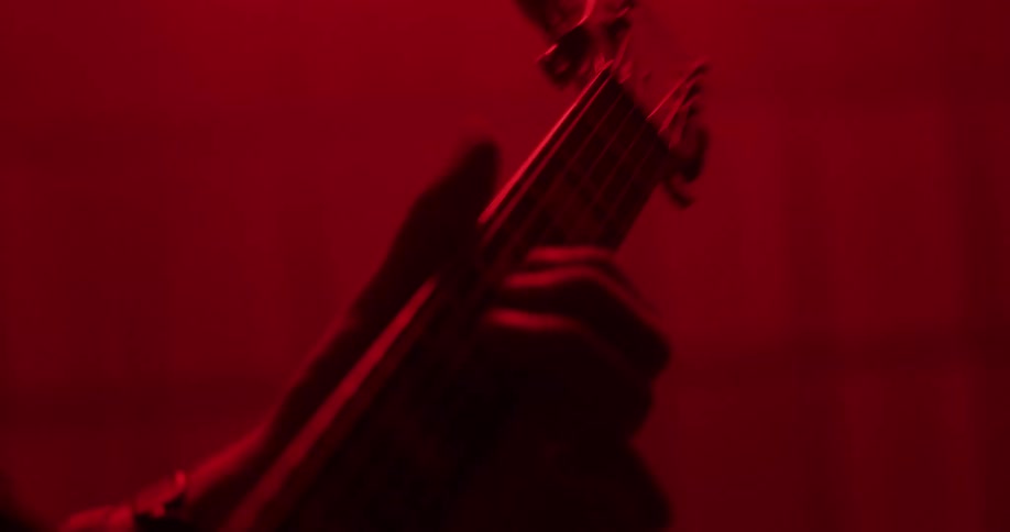 Silhouetted long-haired musician passionately plays an electric guitar and headbangs in a hazy room under dramatic red lighting