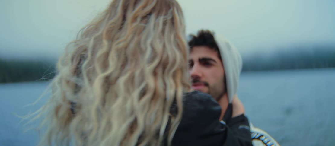 A close-up of a romantic couple sharing an intimate moment while embracing by a lake on a windy, overcast day