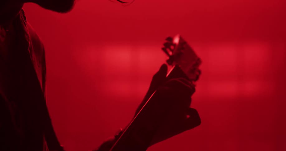 Silhouette of a guitarist playing a passionate solo on an electric guitar under intense red stage lights