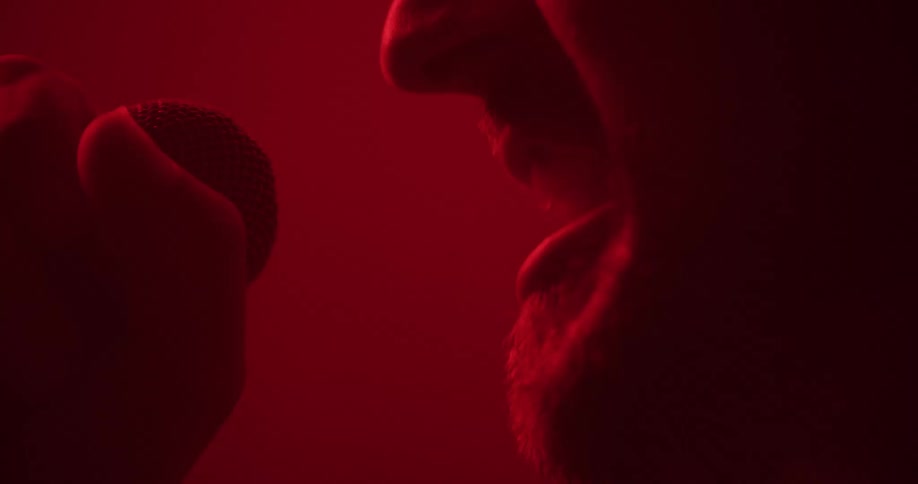 An extreme close-up silhouette of a singer passionately performing into a microphone in a studio with dramatic red lighting