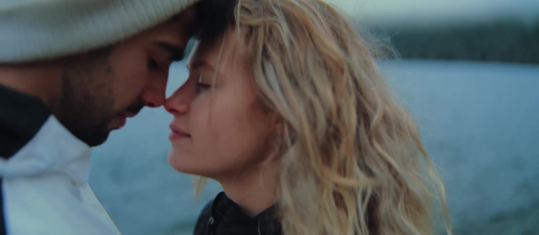 A loving couple shares a tender, intimate moment with foreheads together by the water on a cool day