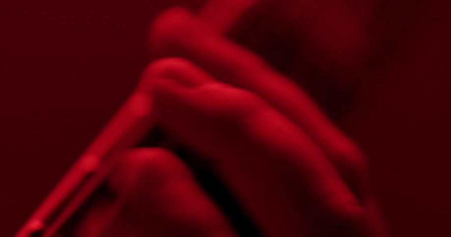 Close-up of fingers rapidly playing chords on a guitar fretboard, bathed in moody red light