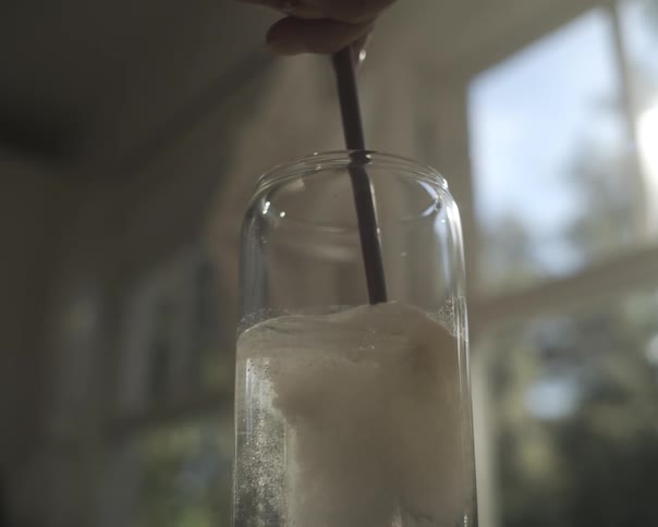 A close-up shot of an effervescent tablet fizzing and dissolving in a glass of water with a wooden spoon inside