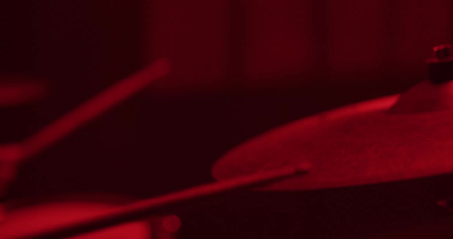 Slow motion close-up of a drummer's hand hitting a hi-hat cymbal with a drumstick in a dark room under dramatic red light