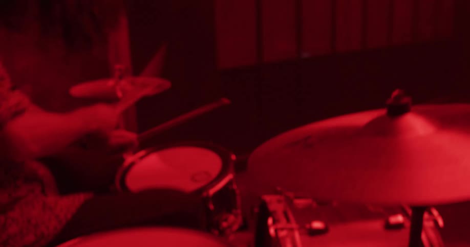 A musician plays the drums with passion and energy in a studio filled with moody red light