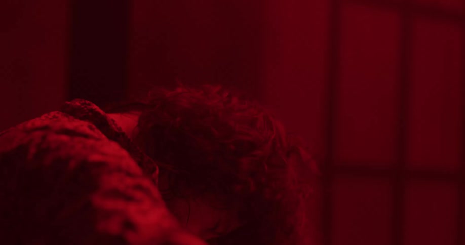An energetic drummer with shaggy hair performs a solo on a drum kit under intense red lighting in slow motion