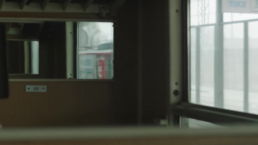 Interior view from a moving train car shows another train passing by in the reflection as it pulls away from the station