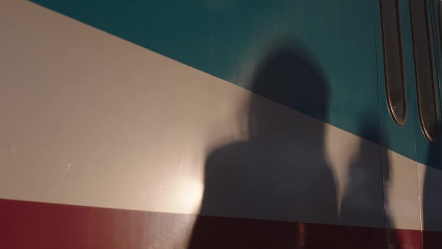 Abstract shadows of waiting commuters dance across the colorful exterior of a train car at sunset