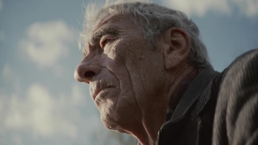 A dramatic low-angle close-up reveals the contemplative face of an elderly man as it comes into focus