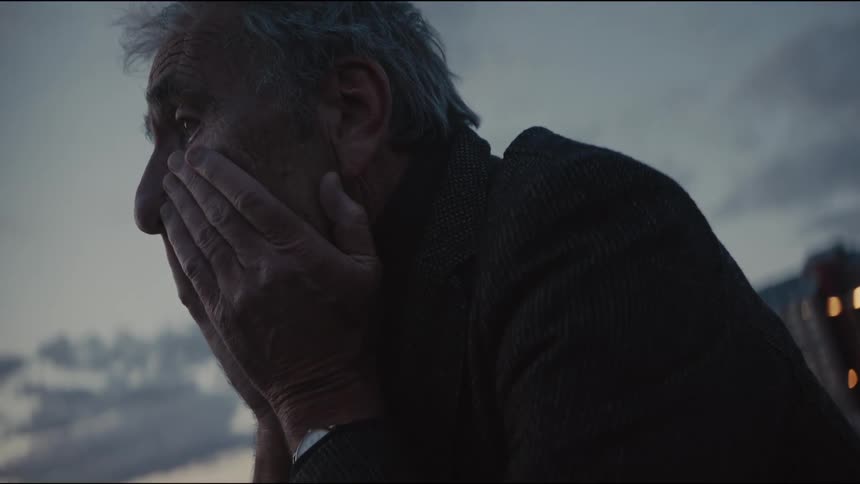 A distraught elderly man covers his face with his hands in despair against a cloudy evening sky