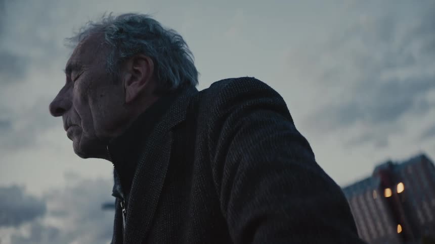 A low-angle close-up of a contemplative elderly man closing his eyes and finding a moment of peace outdoors at dusk