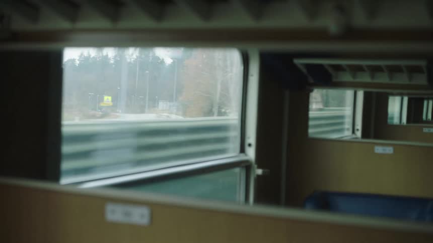 An out-of-focus view from an empty train compartment looking out the window as the landscape and a parallel highway pass by