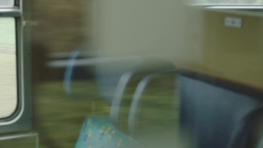 Blurry, abstract view from inside a speeding train showing empty seats and the passing landscape in reflection