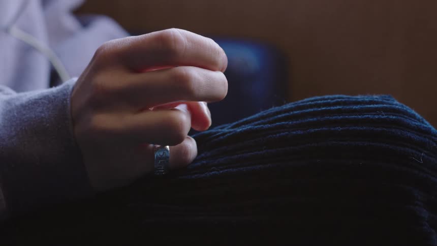 A moody close-up of a person's hand with a silver ring resting on their knee