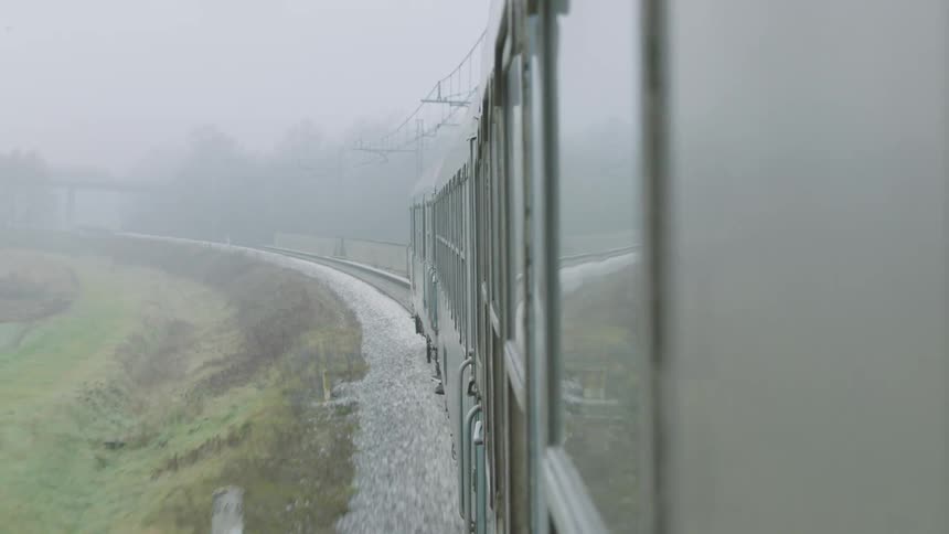 Side view of a passenger train curving along the tracks through a dense foggy rural landscape