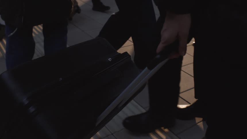 Low-angle slow-motion view of travelers with luggage waiting on a train station platform during golden hour