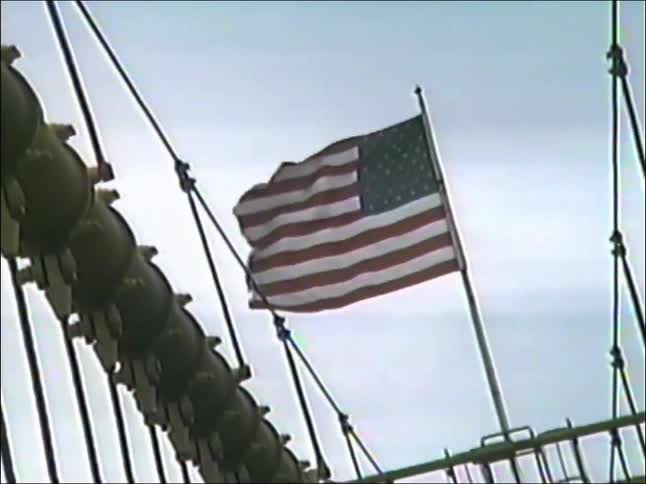 A slow zoom from a vintage camcorder reveals the American flag waving atop the iconic Brooklyn Bridge in New York City