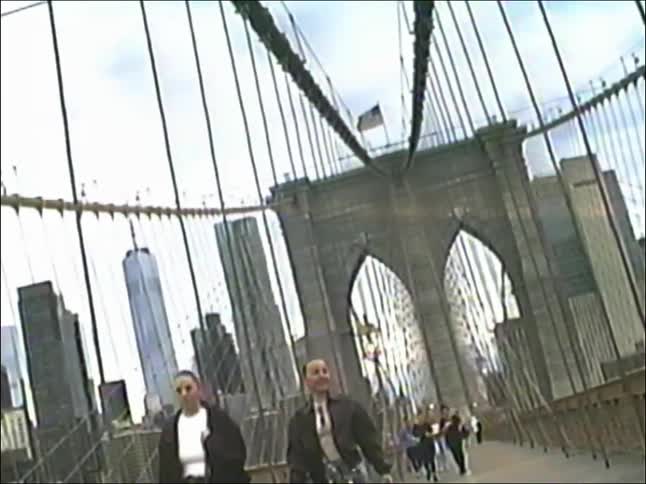 Low-angle vintage-style shot of joggers and pedestrians on the Brooklyn Bridge with the New York City skyline in the background