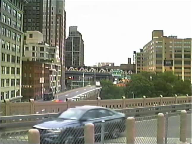 Vintage camcorder footage captures city traffic flowing over a highway overpass on a hazy day