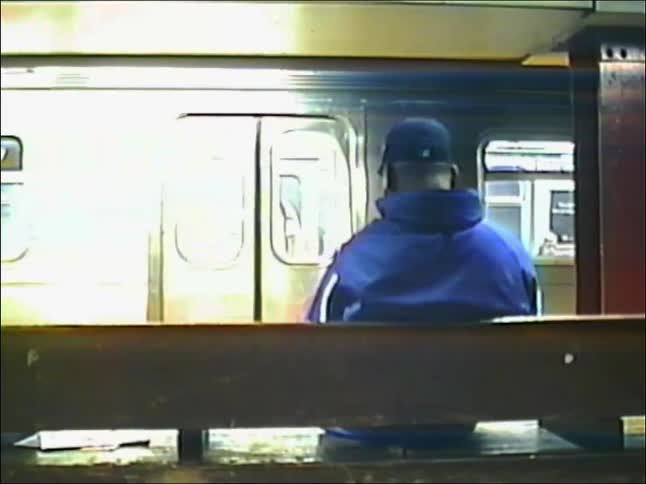 Grainy VHS footage captures a man waiting on a subway platform as a train arrives, passengers disembark, and another train approaches
