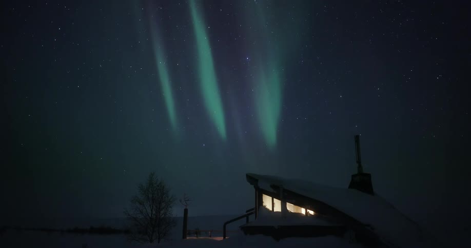 A stunning aurora borealis illuminates the starry night sky above a modern, snow-covered cabin in a winter landscape