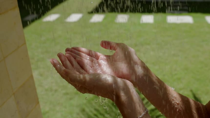Close-up of a woman's hands catching refreshing water from an outdoor shower on a sunny day in slow motion