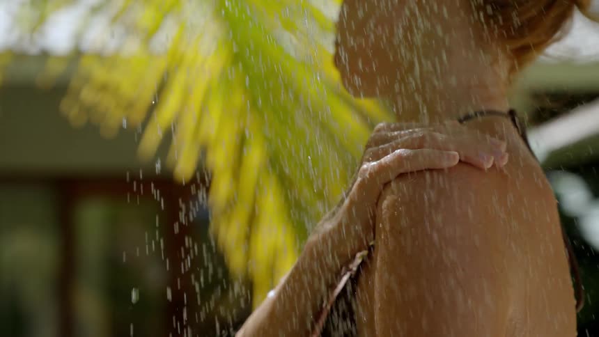 Slow motion close-up of a woman's shoulder as she enjoys a refreshing outdoor shower in a lush tropical setting