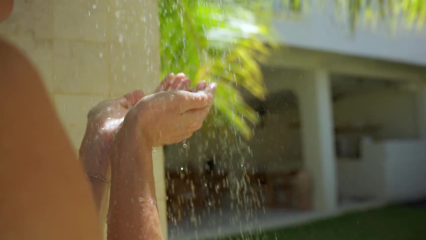 Slow motion close up of a person catching water in their hands from an outdoor shower in a tropical setting