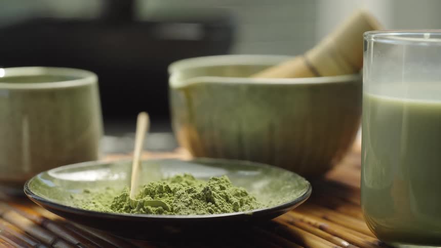 A serene, sunlit scene reveals matcha powder and traditional preparation tools alongside a freshly made matcha latte