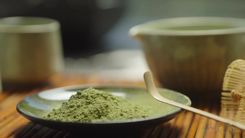 A serene, close-up dolly shot reveals a traditional Japanese matcha tea ceremony set, including powder, a bamboo whisk, and ceramic bowls on a mat