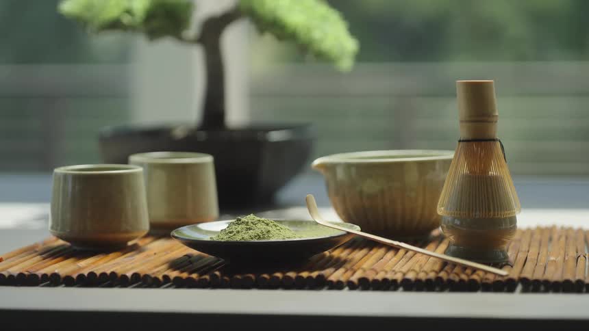 A beautifully arranged traditional Japanese matcha tea set sits on a bamboo mat, ready for a serene ceremony