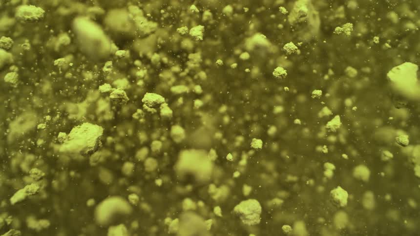 Abstract macro shot of yellow green powder particles suspended and floating upwards in slow motion