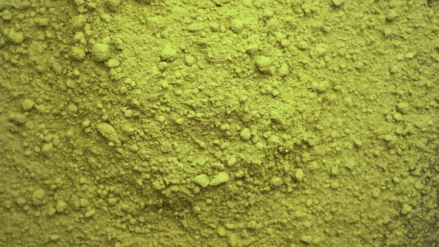 A macro top-down view of vibrant yellow-green matcha tea powder slowly pulling back to reveal its fine texture