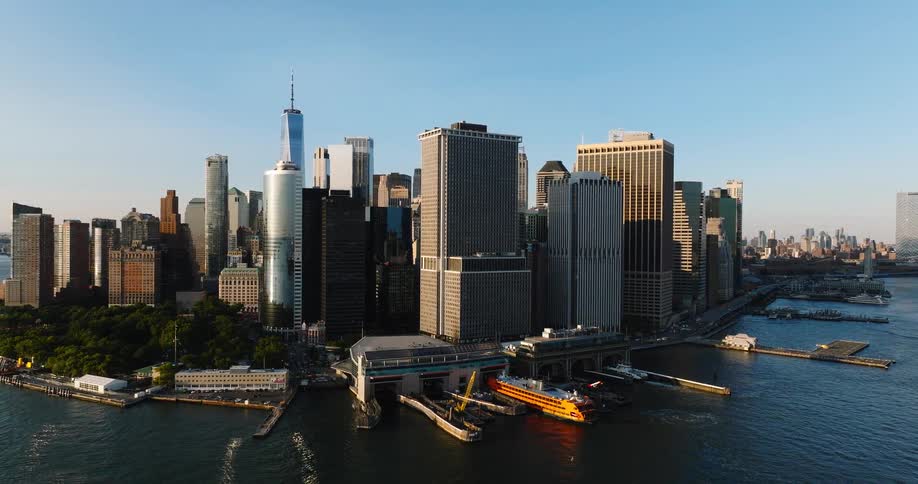 A stunning aerial view reveals the iconic Lower Manhattan skyline and the Staten Island Ferry terminal on a bright sunny day