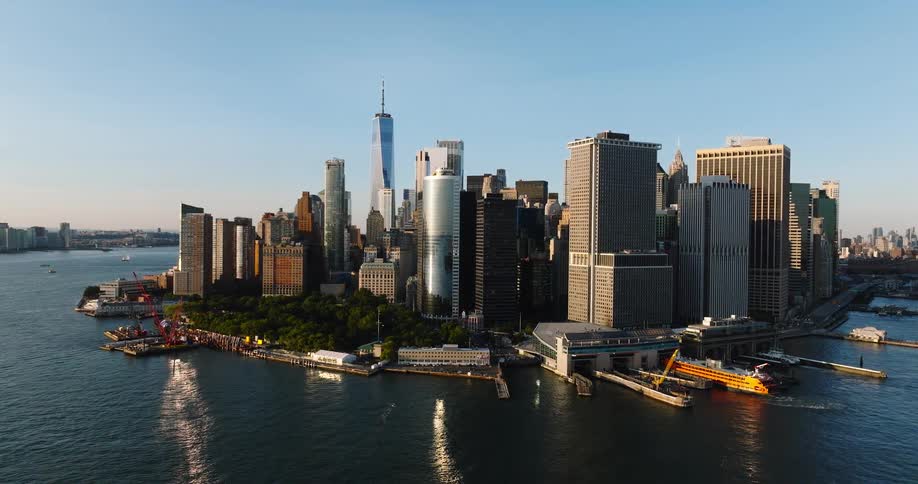 An aerial shot of the lower Manhattan skyline in New York City with the One World Trade Center against a clear blue sky at sunset