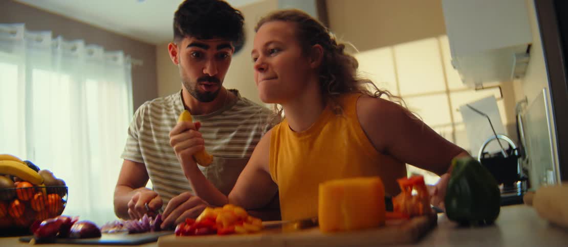 A playful young couple has fun singing and dancing while preparing a healthy meal together in their sunlit kitchen
