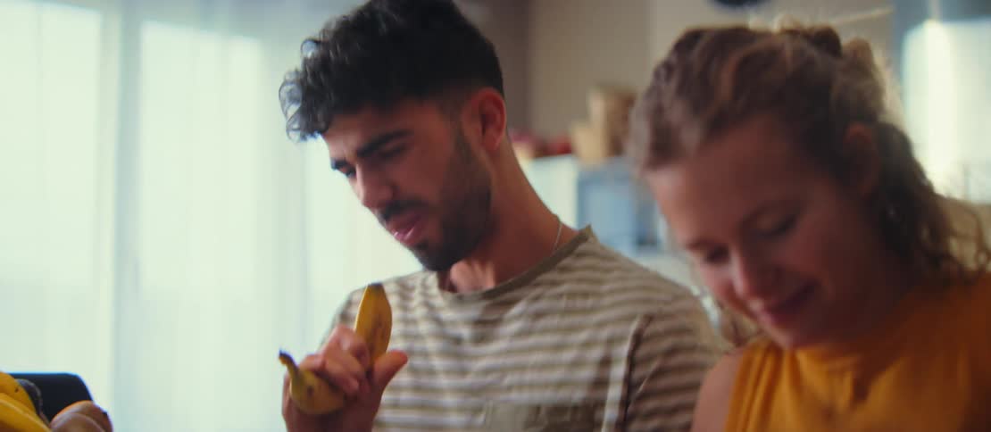 A joyful young couple goofs around and sings together in their kitchen, using a banana as a microphone