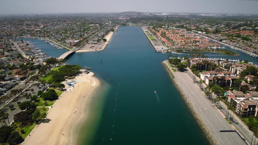 A high-angle aerial view captures a beautiful coastal community's marina, waterways, and sandy beach on a sunny day