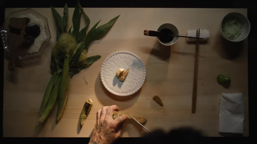 Artistic overhead shot of a chef's tattooed hands slicing fresh corn for a gourmet meal