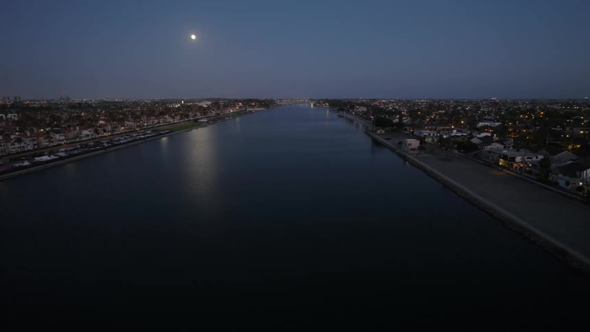 A beautiful, still aerial shot of a tranquil water channel at dusk with a full moon shining in the clear night sky