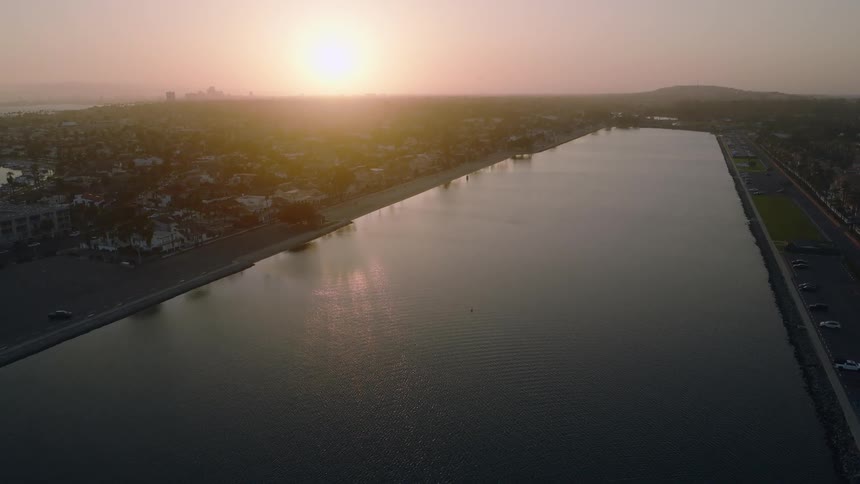 A serene aerial view captures the golden sunset reflecting on a calm bay next to a coastal city