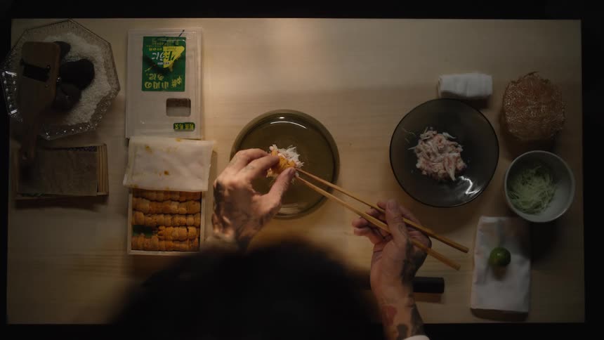 Overhead slow-motion shot of a tattooed chef carefully plating a delicate dish with fresh sea urchin and crab meat