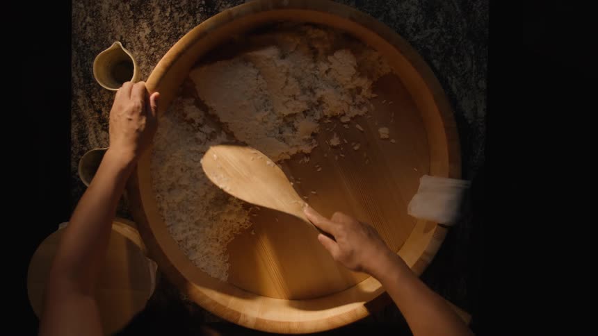 A chef carefully mixes and cools traditional sushi rice in a wooden hangiri bowl in this dramatic top-down slow-motion shot