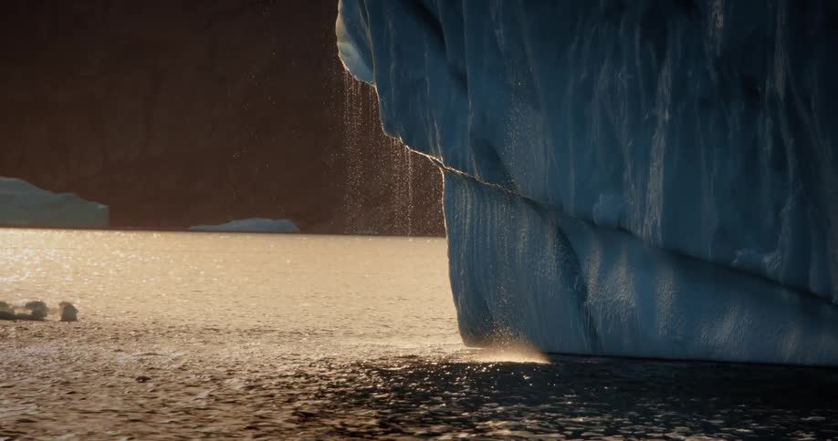 A massive iceberg melts under the golden sunset, creating a small waterfall that glistens as it falls into the arctic sea