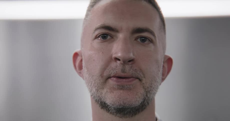 Close-up of a serious middle-aged man with a goatee looking at the camera, then briefly glancing away