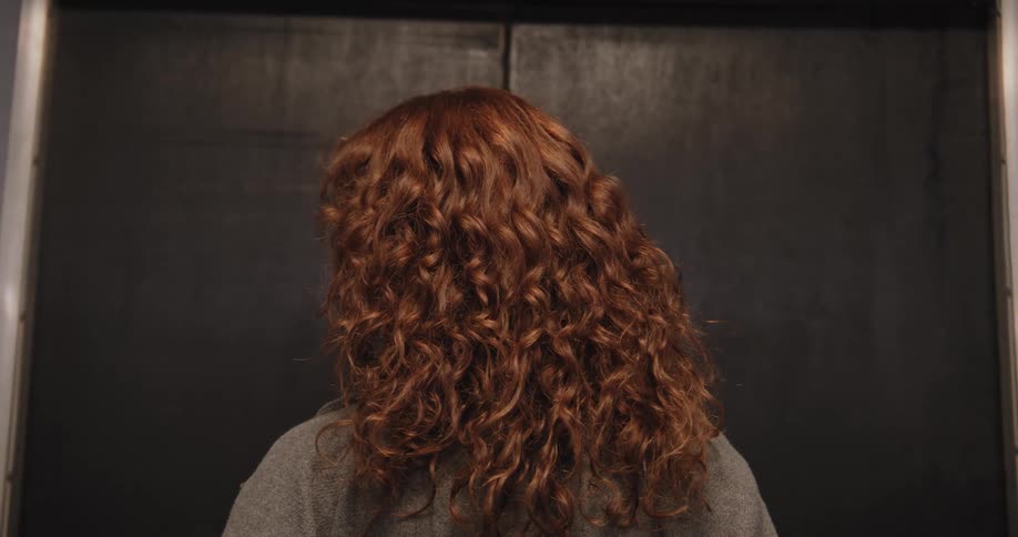 Back view of a woman with long curly red hair as the elevator doors close in front of her