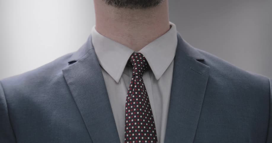 Slow motion close-up of a professional man in a grey suit carefully adjusting his dark polka dot tie