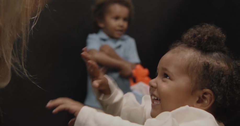 An adorable toddler girl with curly hair smiles with pure joy while playing a clapping game with an adult